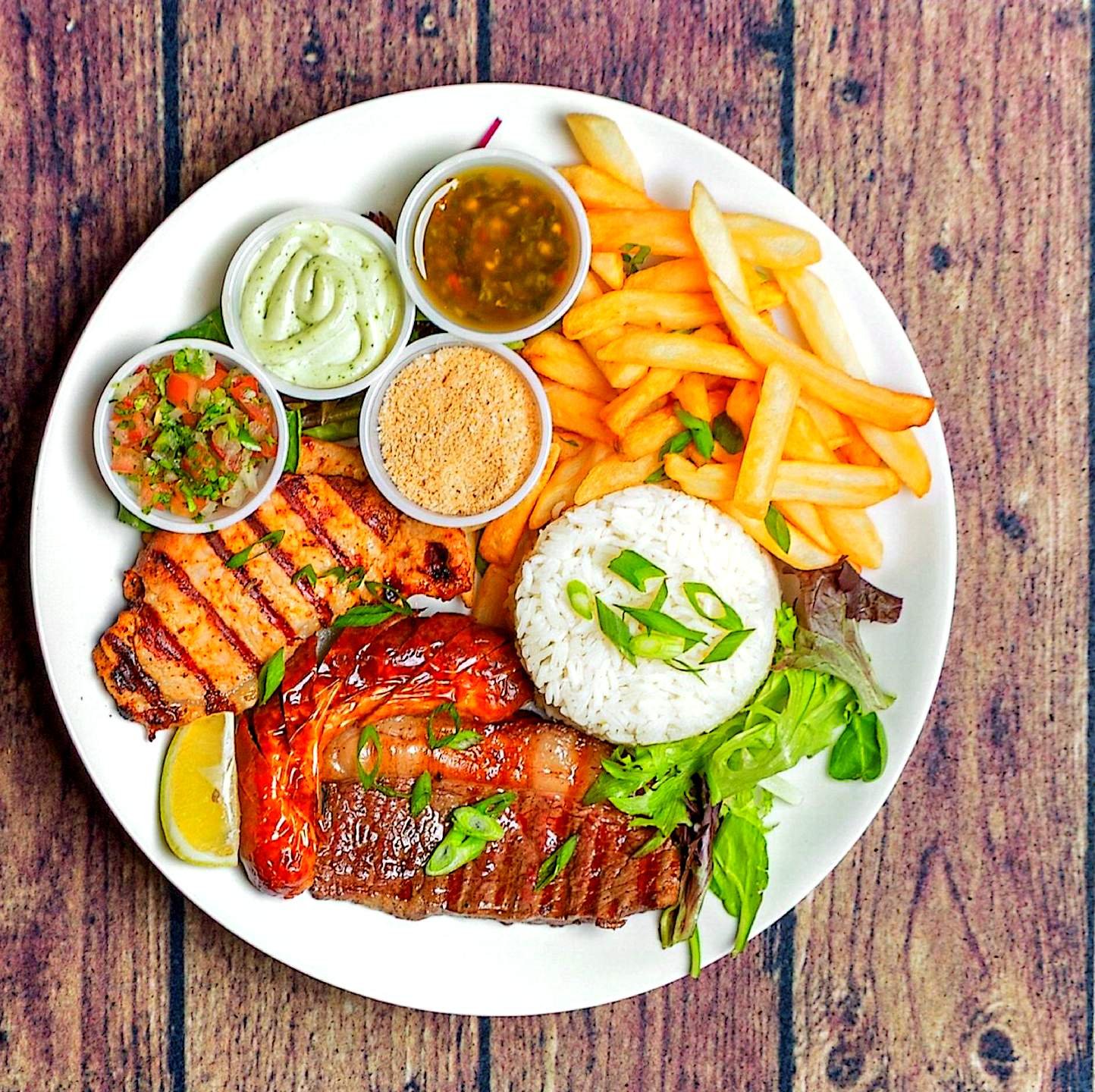 Brazilian mixed grill plate with steak, chicken, sausage, rice, fries, and sauces