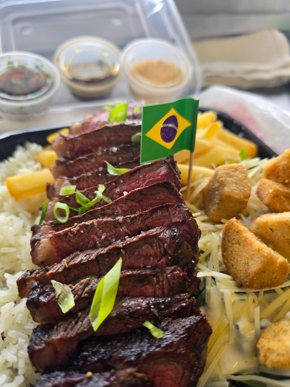 Takeaway Brazilian steak plate with golden bites and a Brazilian flag