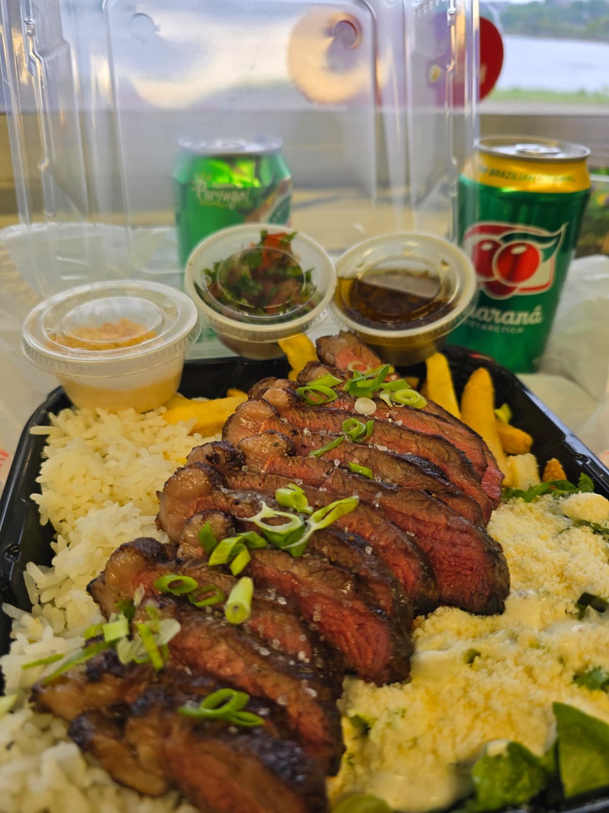 An Eduardo's takeaway steak plate with rice, sides, sauces, and Guaraná